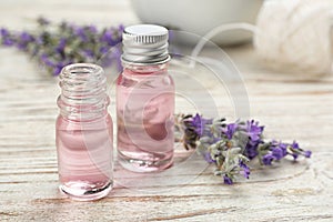 Bottles with natural lavender oil and flowers on white wooden table. Space for text