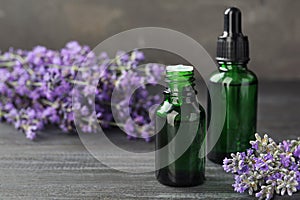Bottles with natural lavender oil and flowers on wooden table against grey background. Space for text