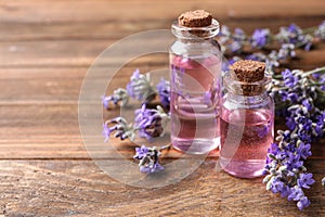 Bottles with natural lavender oil and flowers on wooden table, closeup view