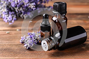 Bottles with natural lavender oil and flowers on wooden table. Space for text