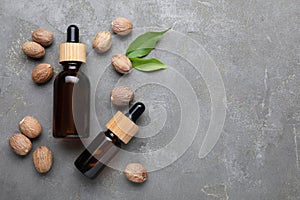 Bottles of nutmeg oil and nuts on grey table, flat lay. Space for text