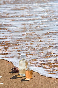 Bottles with oil essence and shell in the sea waves. Spa and wellness setting on sand and wave background.   Manicure and Pedicure