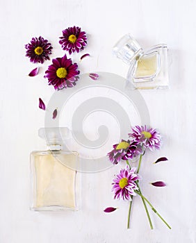 Bottles of perfume and flowers on white wooden background.