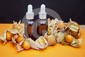 Bottles with physalis oil  and fresh  fruit  on orange