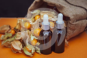 Bottles with physalis oil  and fresh  fruit  on orange