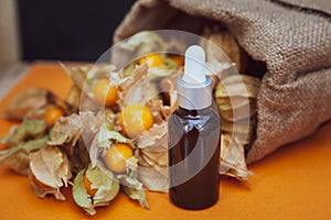 Bottles with physalis oil  and fresh  fruit  on orange