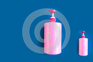 Bottles with pink dishwashing liquid on blue background. Minimal concept.