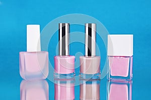 Bottles of pink nail Polish on a mirror surface on a blue background