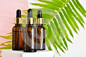 Bottles with pipettes of cosmetics on white podium on a pink background with fern leave. Bath accessories