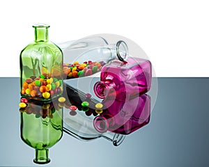 Bottles of rectangular shape made of colored glass filled with sweets are reflected in the mirror surface. Abstract