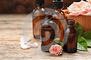 Bottles of rose essential oil and flowers on wooden table