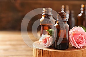 Bottles of rose essential oil and fresh flowers on table, closeup