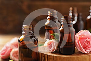 Bottles of rose essential oil and fresh flowers on table