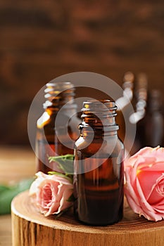 Bottles of rose essential oil and fresh flowers on table, closeup