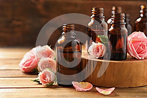 Bottles of rose essential oil and fresh flowers on wooden table