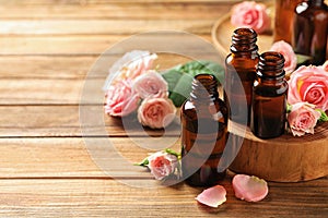 Bottles of rose essential oil and fresh flowers on wooden table