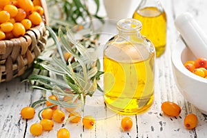 Bottles of sea buckthorn essential oil, mortar and basket of sandthorn berries