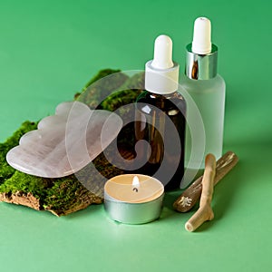 Bottles of Serum and Gua Sha Gem on Tree Bark Green Background Moisturizer Vitamin C Hyaluronic acid Beauty Concept