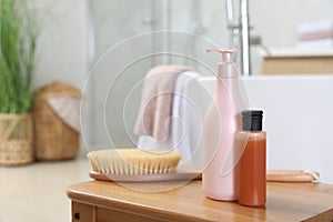 Bottles of shower gels and brush on wooden table near tub in bathroom, space for text