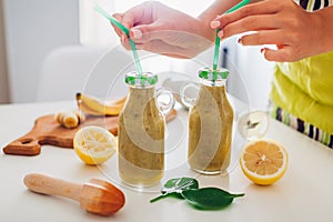 Bottles with spinach and banana smoothie with ingredients. Woman puts straws in drinks. Healthy detox diet