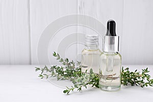 Bottles of thyme essential oil and fresh plant on white wooden table, space for text