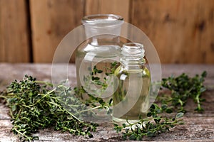 Bottles of thyme essential oil and fresh plant on wooden table