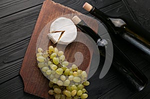 Bottles of wine on a black wooden background with grapes and cheese Camemberg.