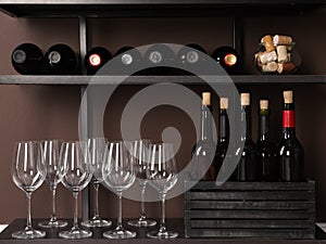 Bottles of wine, corks and glasses on rack near brown wall