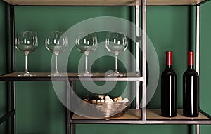Bottles of wine, corks and glasses on rack near green wall
