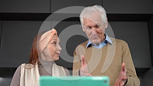 Bottom angle view of smiling senior Caucasian man and woman waving talking smiling standing in kitchen indoors