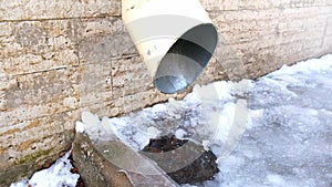 The bottom of a drainpipe with dripping snow melting