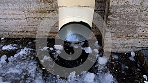 The bottom of a drainpipe with dripping snow melting