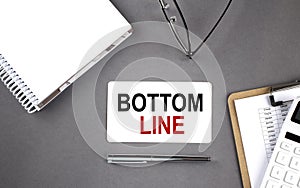 BOTTOM LINE text written on the card with notebook and clipboard, grey background