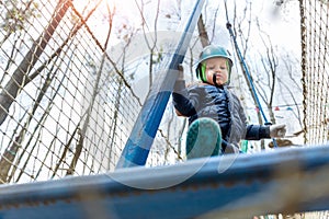 Bottom POV view brave courage little toddler child boy wear safety equipment helmet enjoy passing obstacle course forest