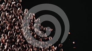 From the bottom up, many black roasted coffee beans fly up on a black background