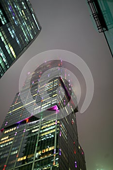 A bottom-up view of the facade of a modern office building at night in fog. Light of the night city. Moscow City