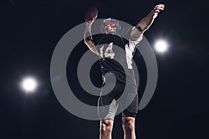 bottom view of american football player throwing ball under spotlights