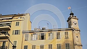 Bottom view of an ancient clock tower and a yellow residential old building on blye sky background. Action. Concept of