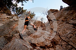 bottom view of athletic young woman who skilfully climbing up on rocks using rope.