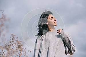 Bottom view of attractive brunette Caucasian young woman traveler with windy hair, posing against overcast sky. Dreamy female with