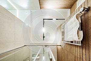 Bottom view of bathroom interior with glass shower cabin and towel rail. White ceiling with line lamp in the middle