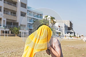 Bottom view on the boy with yellow towel wiping hair after swimming in the sea on the resort town background.