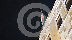 Bottom view of building with flag at night. Action. Building with flag on background of night sky. Beautiful snow falls