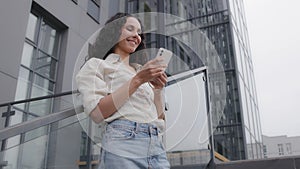 Bottom view Caucasian Hispanic 30s woman in city female tourist businesswoman with phone outdoor typing in smartphone