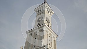 Bottom view of a clock tower with a long spire on blue cloudy sky background. Action. Details of an ancient historical