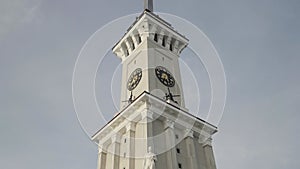 Bottom view of a clock tower with a long spire on blue cloudy sky background. Action. Details of an ancient historical