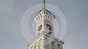 Bottom view of a clock tower with a long spire on blue cloudy sky background. Action. Details of an ancient historical