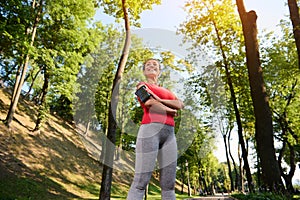 Bottom view of a confident 30 years old pretty woman in sportswear standing in a forest city park with her arms crossed and