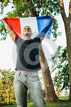 Bottom view cropped portrait of young smiling man holding flag of France isolated over natural background