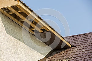 Bottom view detail of new modern house cottage corner with stucco walls, brown shingled roof and unfinished siding installation on